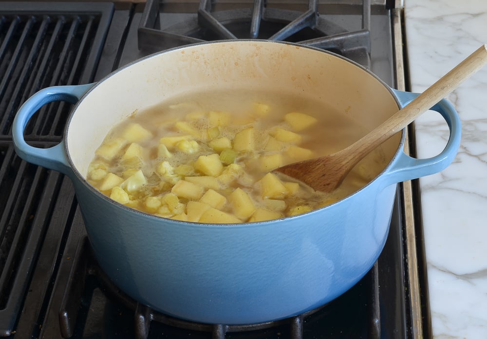 Wooden spoon stirring a pot of broth and vegetables.