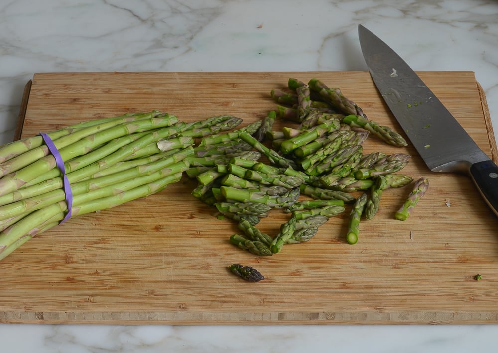 Knife on a cutting board with asparagus tips.
