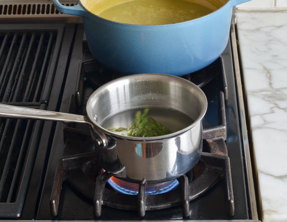 Asparagus tips in a small pot of water.