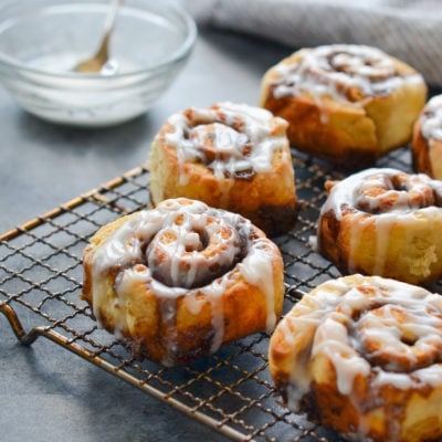 Cinnamon buns with buttermilk glaze on a wired rack.