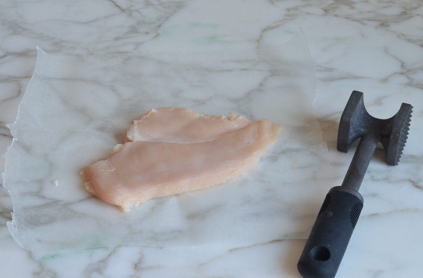 Pounded chicken next to a meat mallet.