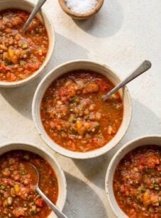 Four bowls of roasted garlic gazpacho on stone table