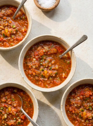Four bowls of roasted garlic gazpacho on stone table