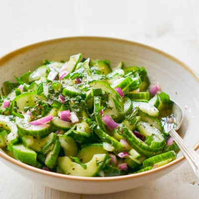 Spoon in a bowl of cucumber salad with mint.