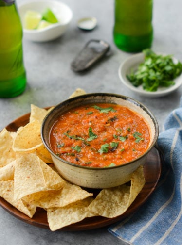 Bowl of roasted tomato salsa on a plate with chips.