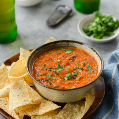 Bowl of roasted tomato salsa on a plate with chips.
