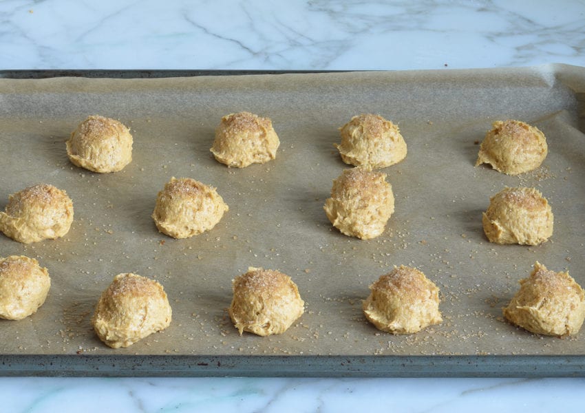Balls of pumpkin cookie dough on a lined baking sheet.