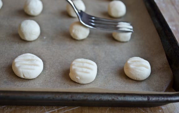 pressing-dough-balls-flat Fork pressing balls of cookie dough on a lined baking sheet.