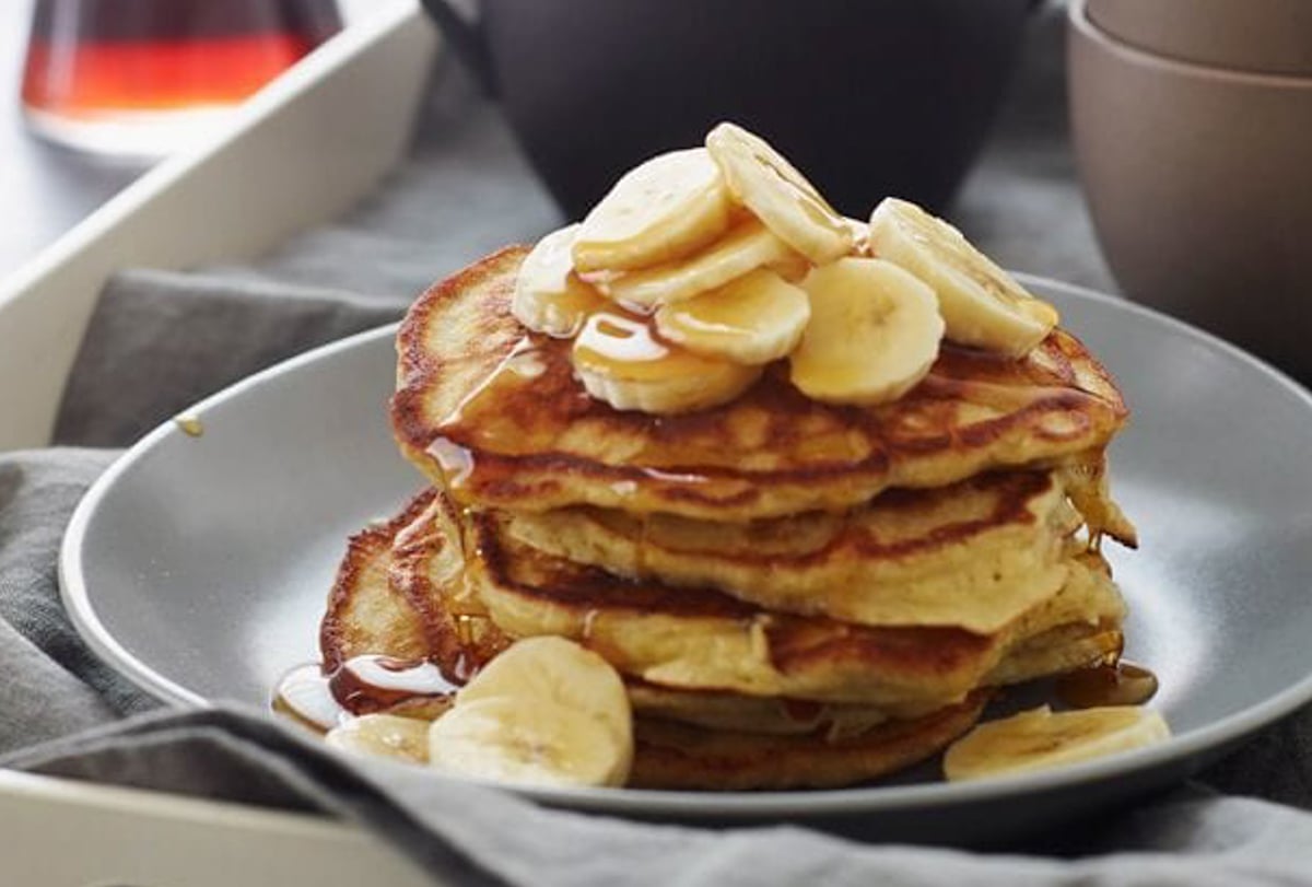 banana pancakes stacked on a plate and topped with sliced bananas.
