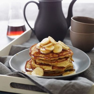 Stack of banana pancakes topped with bananas and syrup.