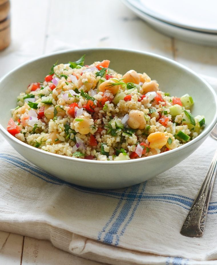 Bowl of bulgur salad with cucumbers, red peppers, chickpeas, lemon, and dill.