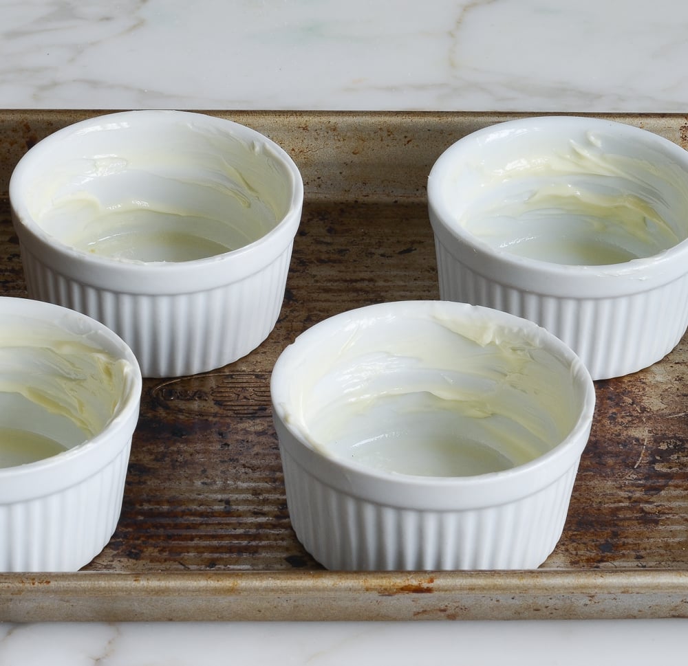Buttered ramekins on a baking sheet.