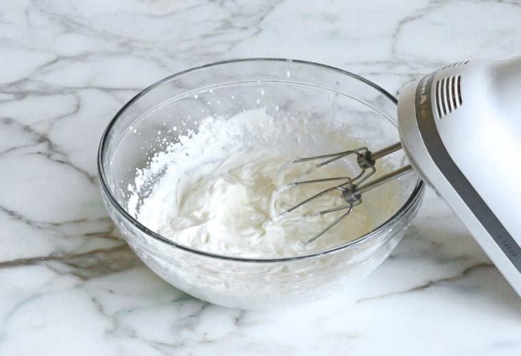 Electric mixer in a bowl of whipped cream.
