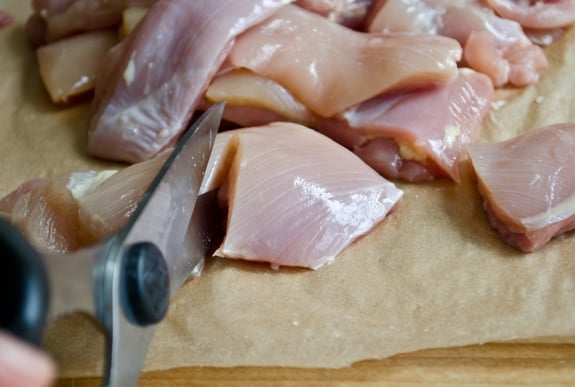 Person using a knife to cut chicken into pieces.