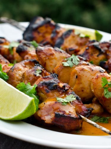 Honey, lime, and sriracha chicken skewers on a plate.