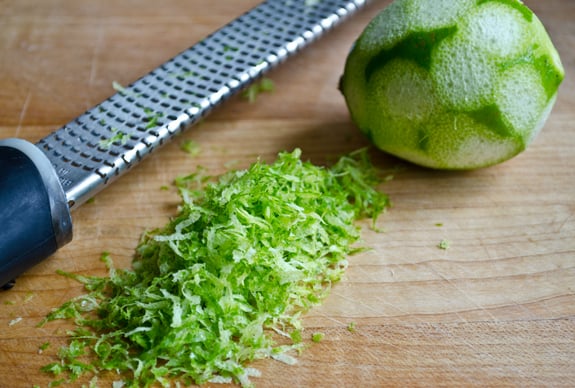 Pile of lime zest with a lime and a micro-plane grater.