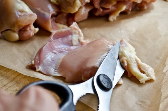 Person using a knife to trim fat from chicken.