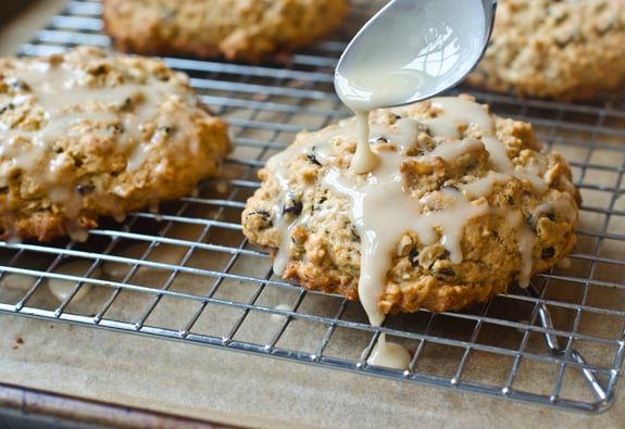 Spoon pouring glaze over oatmeal maple scones with pecans and currants.