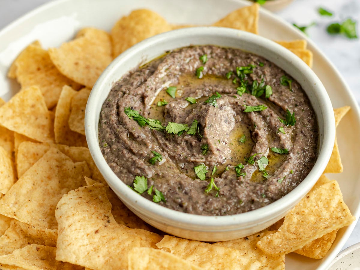 bowl of black bean dip on platter with tortilla chips.