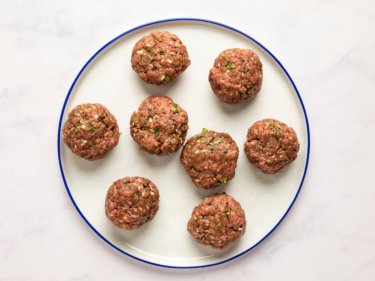 raw meatballs formed on white plate.