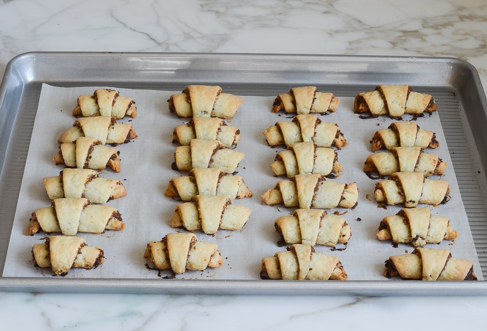 Baked rugelach on a lined baking sheet.