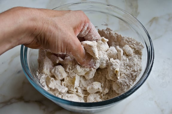 Person rubbing butter into dry ingredients.