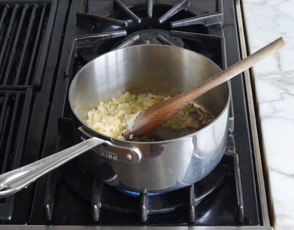 Wooden spoon in a sauce pan with onions.