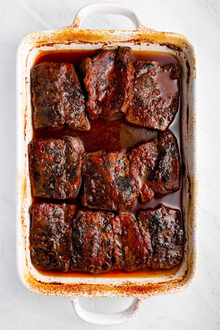 Short ribs in a pan of barbeque sauce.
