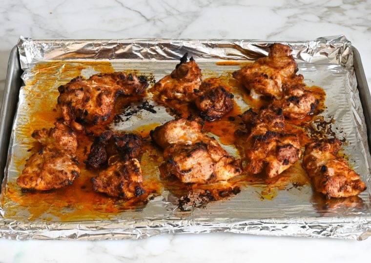Barbeque-spiced chicken thighs on a lined baking sheet.