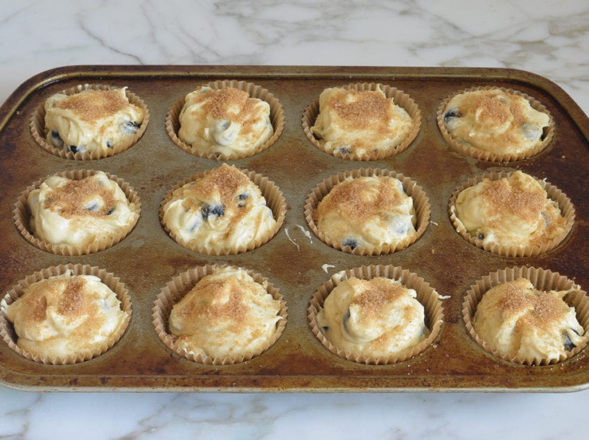 Muffin tin of muffin batter topped with turbinado sugar.