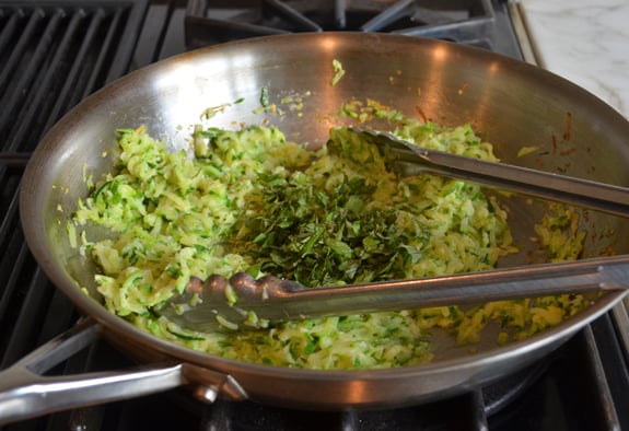 Basil and other seasonings added to a skillet of zucchini.