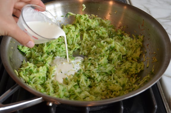 Cream pouring into a skillet of zucchini and garlic.