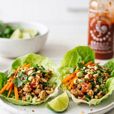Thai chicken lettuce wraps on white plate with Sriracha bottle