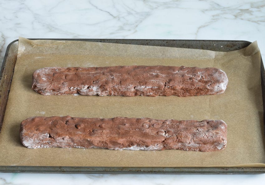 Two long logs of chocolate biscotti dough on a lined baking sheet.