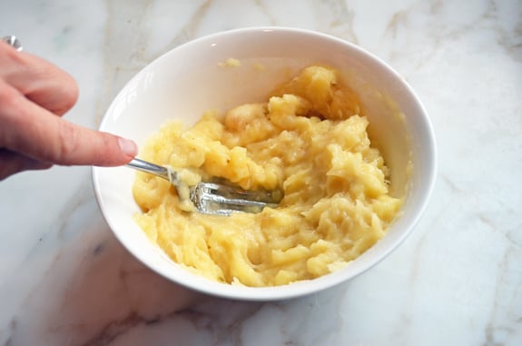 Fork mashing bananas in a bowl.