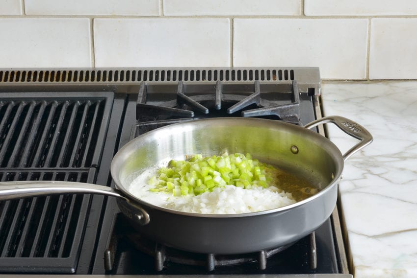 Chopped vegetables cooking in a skillet of melted butter.