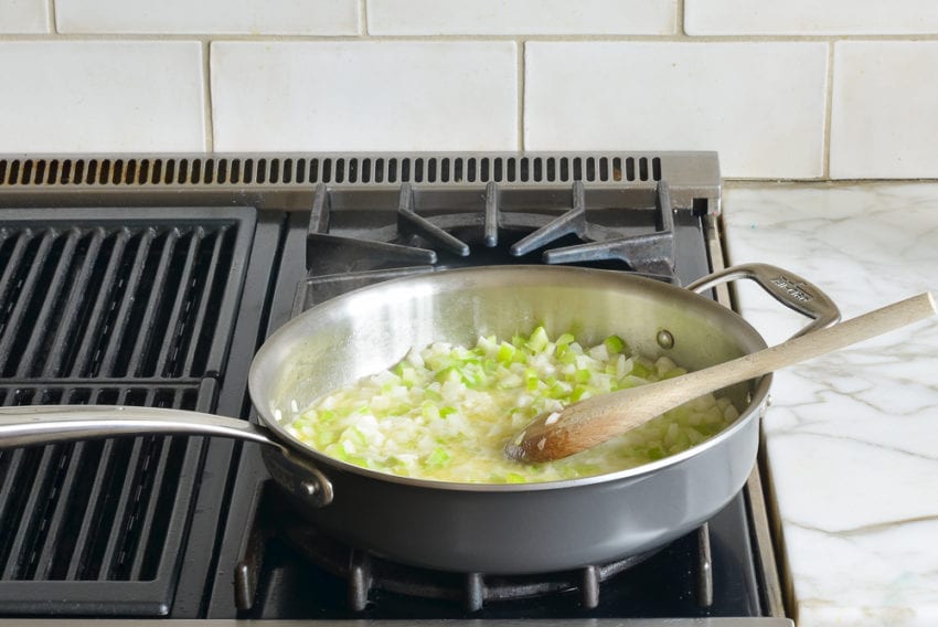 Wooden spoon stirring a skillet of vegetables.