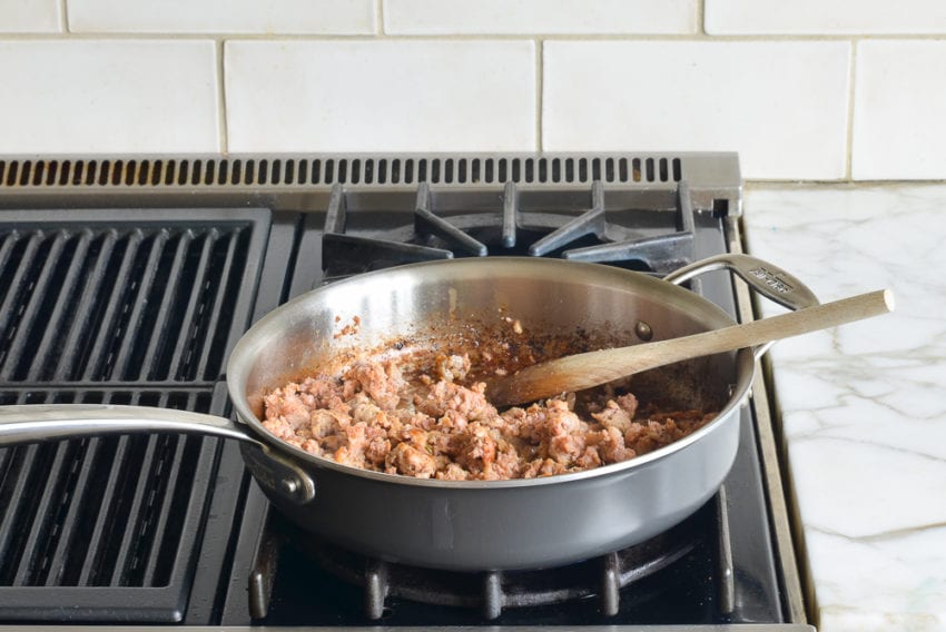 Wooden spoon stirring sausage in a skillet.