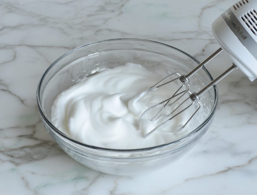 Electric mixer in a bowl with beaten egg whites.