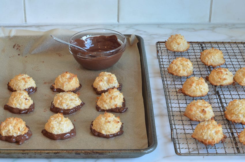 Coconut macaroons dipped in chocolate on a lined baking sheet.