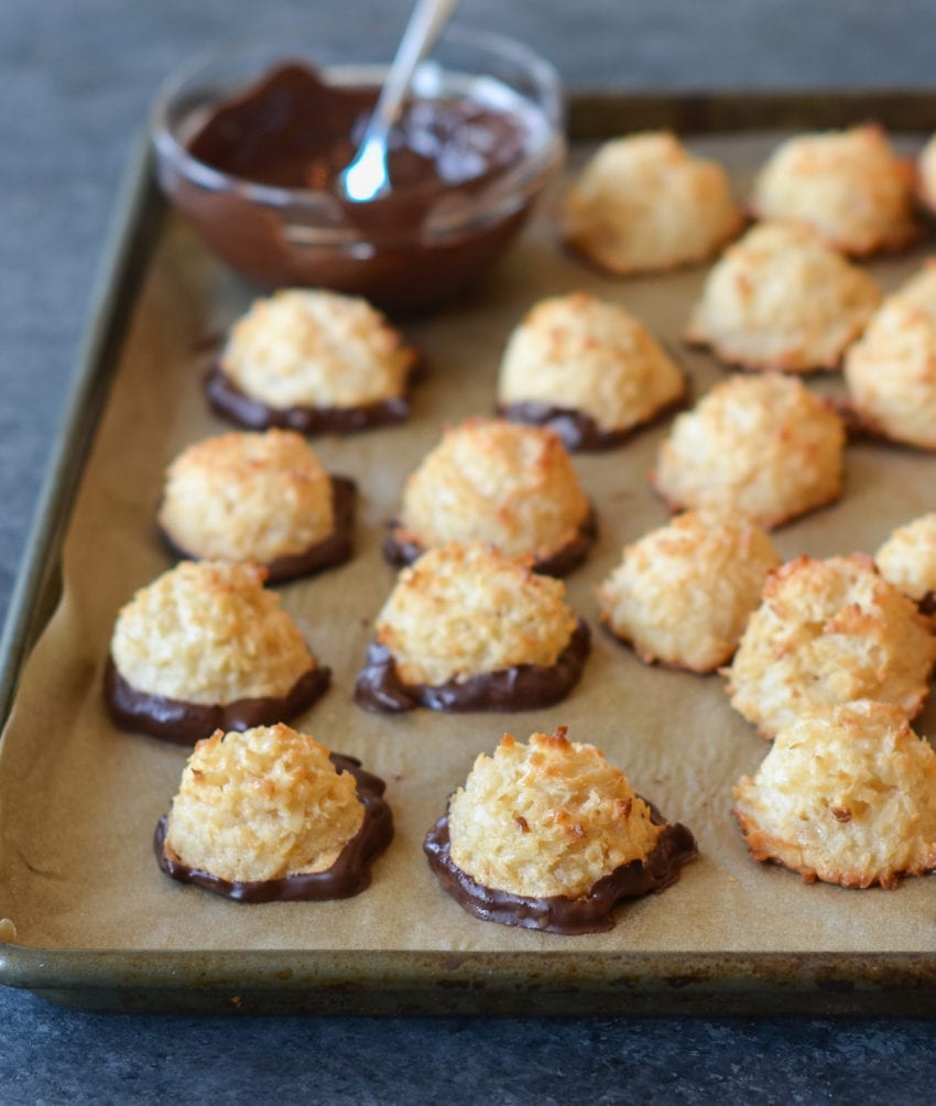 Coconut macaroons dipped in chocolate on a lined baking sheet.