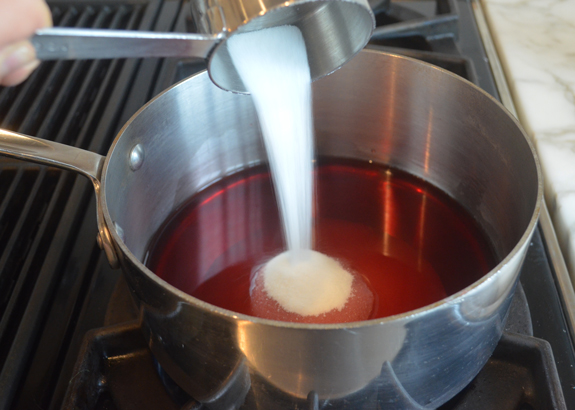 Sugar pouring into a saucepan of pomegranate juice.