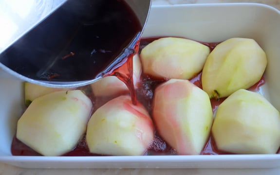 Pomegranate syrup pouring over halved and peeled pears.