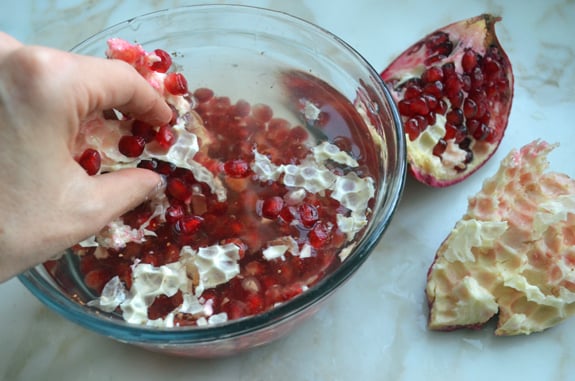 Person removing pomegranate arils in a bowl of water.