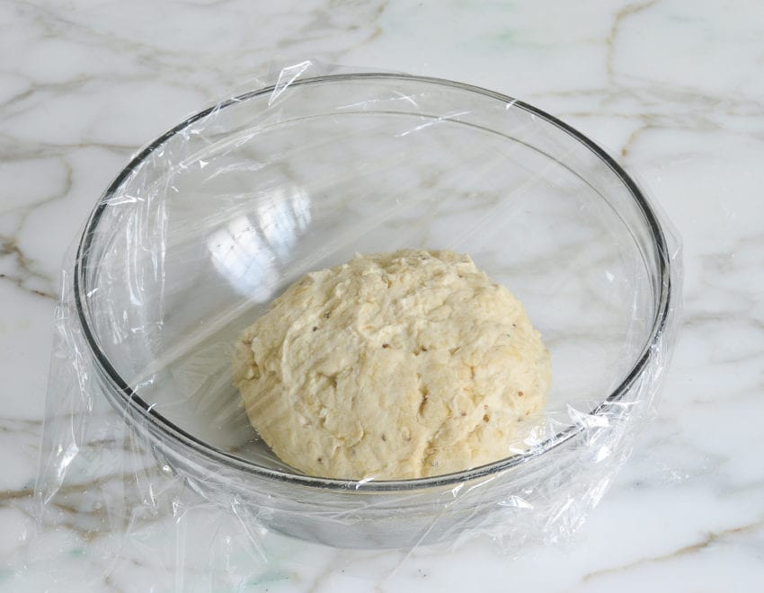 Ball of dough in a bowl covered with plastic wrap.