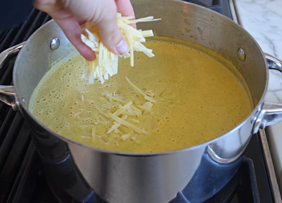 Person adding cheese to soup.