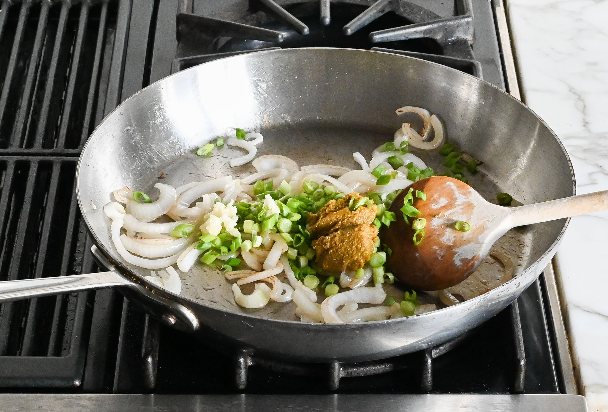 Adding scallions, garlic, and green curry paste to the skillet.