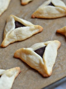 Chocolate-filled hamantaschen on a lined baking sheet.