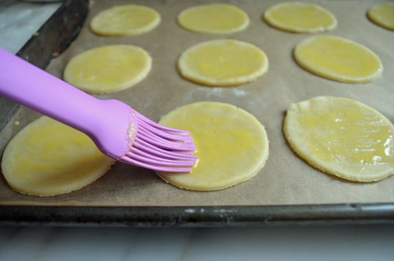 Brush brushing egg wash over small circles of dough.