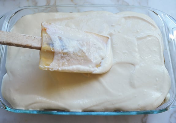 Spatula spreading mascarpone cream in a baking dish.